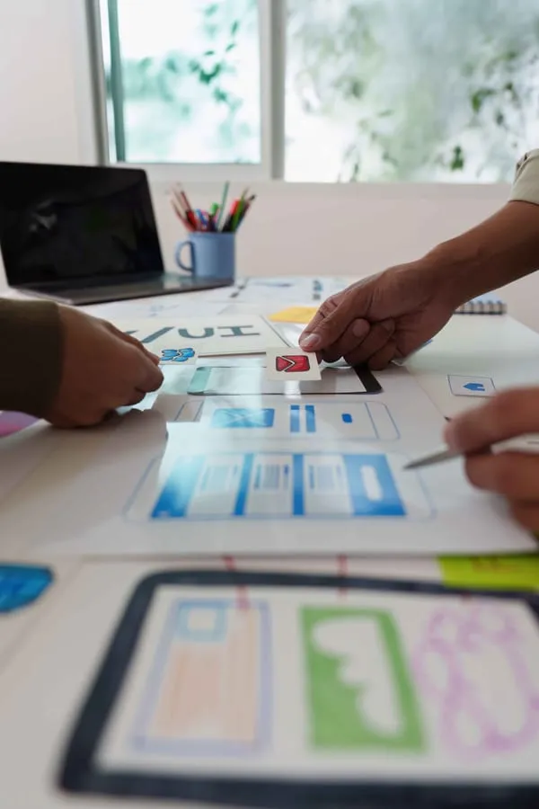 Hands arranging interface wireframes across a workshop table